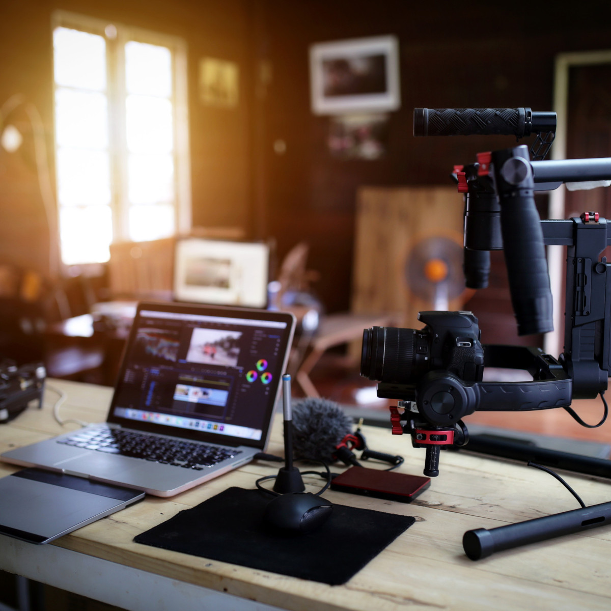 Laptop mit Videoschnittprogramm auf einem Schreibtisch, daneben Kamera auf Gimbal 