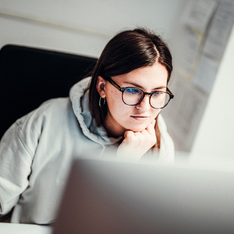 Junge Frau mit Brille schaut konzentriert auf den Bildschirm